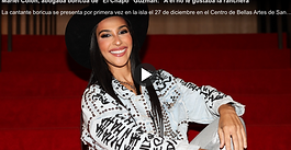 Mariel La Abogada sonriente sentada en unas gradas rojas, vistiendo sombrero negro y chaqueta de mezclilla con detalles gráficos, en un contexto de entrevista o reportaje cultural.