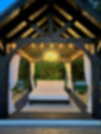 White outdoor bed under with ambient evening lighting under a pool cabana at The Black Swamp Bunkhouse.