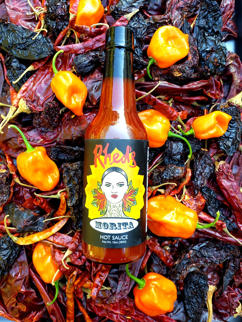 Bottle of Rhed's Morita hot sauce sitting on an abundance of fresh and dried chili peppers.
