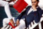 Man in blue suit sits on a lounge chair by water, looking thoughtful. A red handbag and red shoes add vibrant contrast.