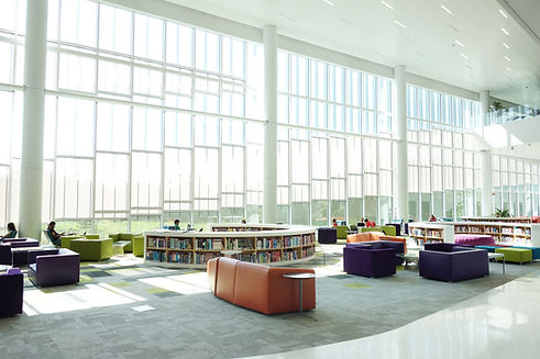 A vibrant library featuring colorful chairs and tables arranged near large windows, inviting natural light.
