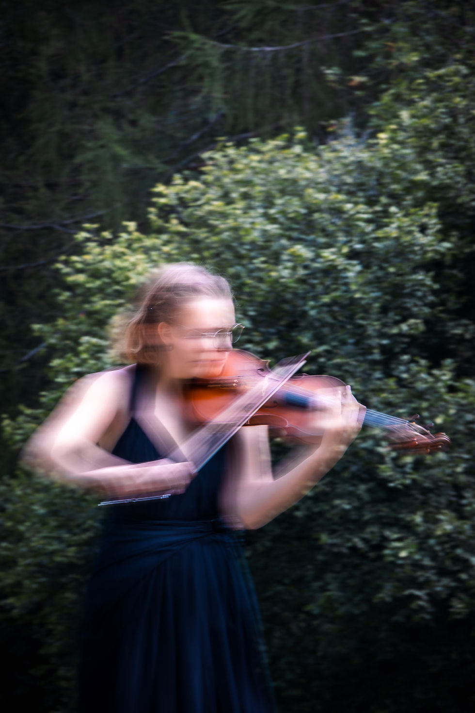 Eine Geigerin die in der Natur spielt. Durch einen Longtime-Exposure ist die Bewegung von der Geigerin verzehrt.