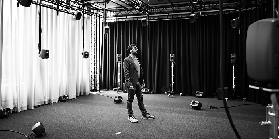 Schwarz-weißes Bild von Sascha Etezazi, der in einem Aufnahmestudio zwischen Lautsprechern und Mikrofonen steht.