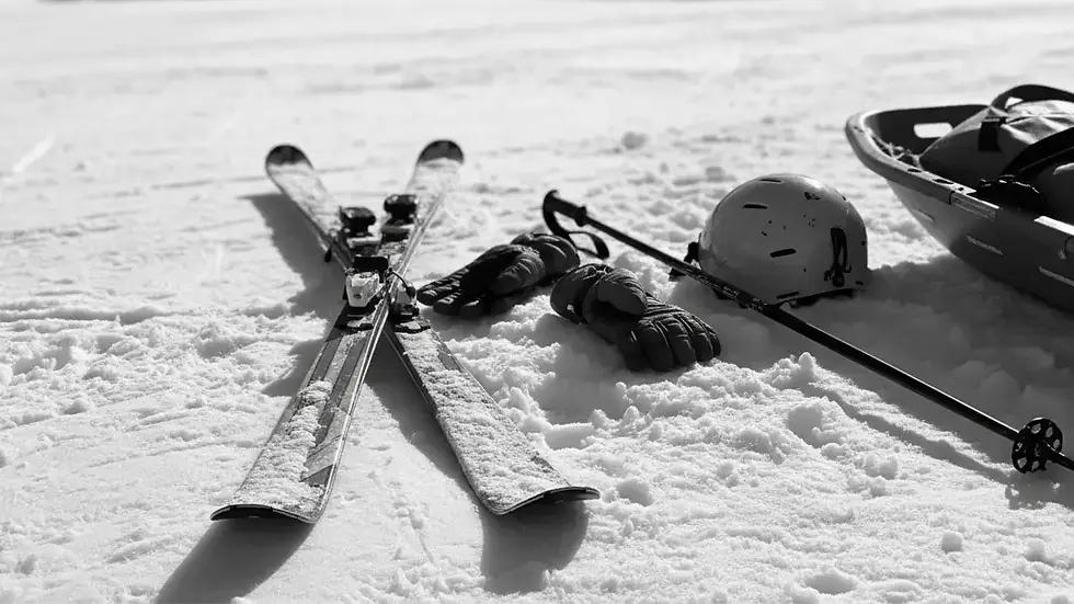 Ego-Perspektive nach Skiunfall: Beine eines Wintersportlers liegen im Schnee, die Skier sind teilweise im Bild. Im unscharfen Hintergrund nähert sich ein Rettungsfahrzeug auf einer beleuchteten Piste.