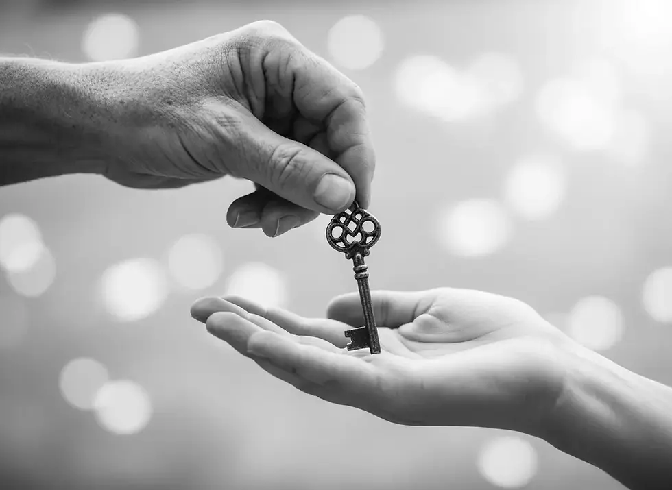 Eine Hand gibt einer anderen einen alten Schlüssel. Der Hintergrund ist unscharf mit Lichtpunkten. Schwarz-Weiß-Foto, symbolisch für vorweggenommene Erbfolge.