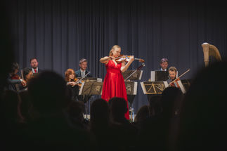 Geigerin in rotem Kleid spielt Solo mit Orchester.