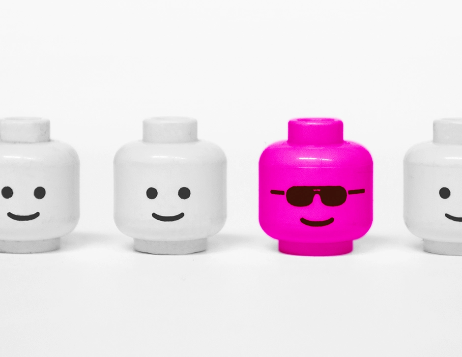 Pink lego head with sunglasses next to other smiling lego heads