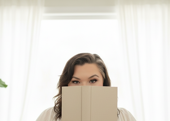 Close-up of author Crystal Lopez holding a light-colored book to her face, surrounded by soft floral tones