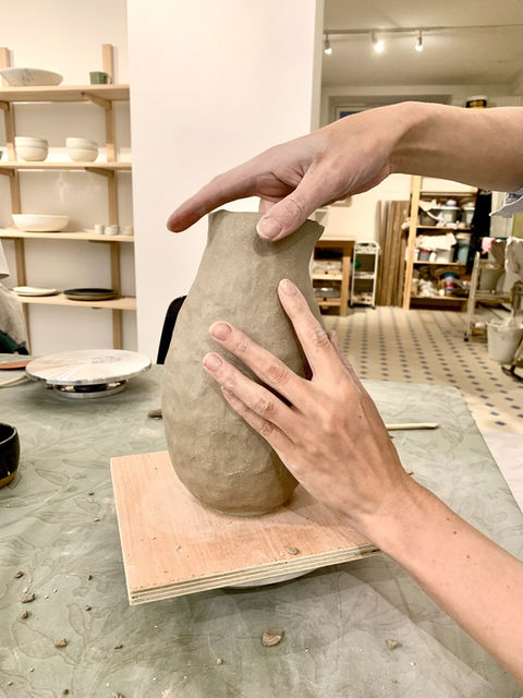 Bildet viser en uferdig håndbygd vase i leire, med verktøy ved siden av.