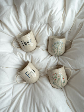 Bildet viser håndlagde kopper i lys leire. Koppene er håndmalt med motiv av "Herr" og Fru", og forglemmegei og markjordbær.
