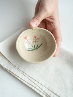 Bildet viser en håndlaget skål i lys leire. Skålen er håndmalt med motiv av strandvikke.