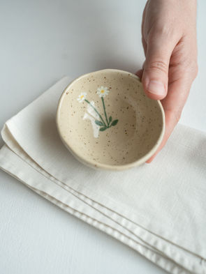 Bildet viser en håndlaget skål i lys leire. Skålen er håndmalt med motiv av fjellroser. 