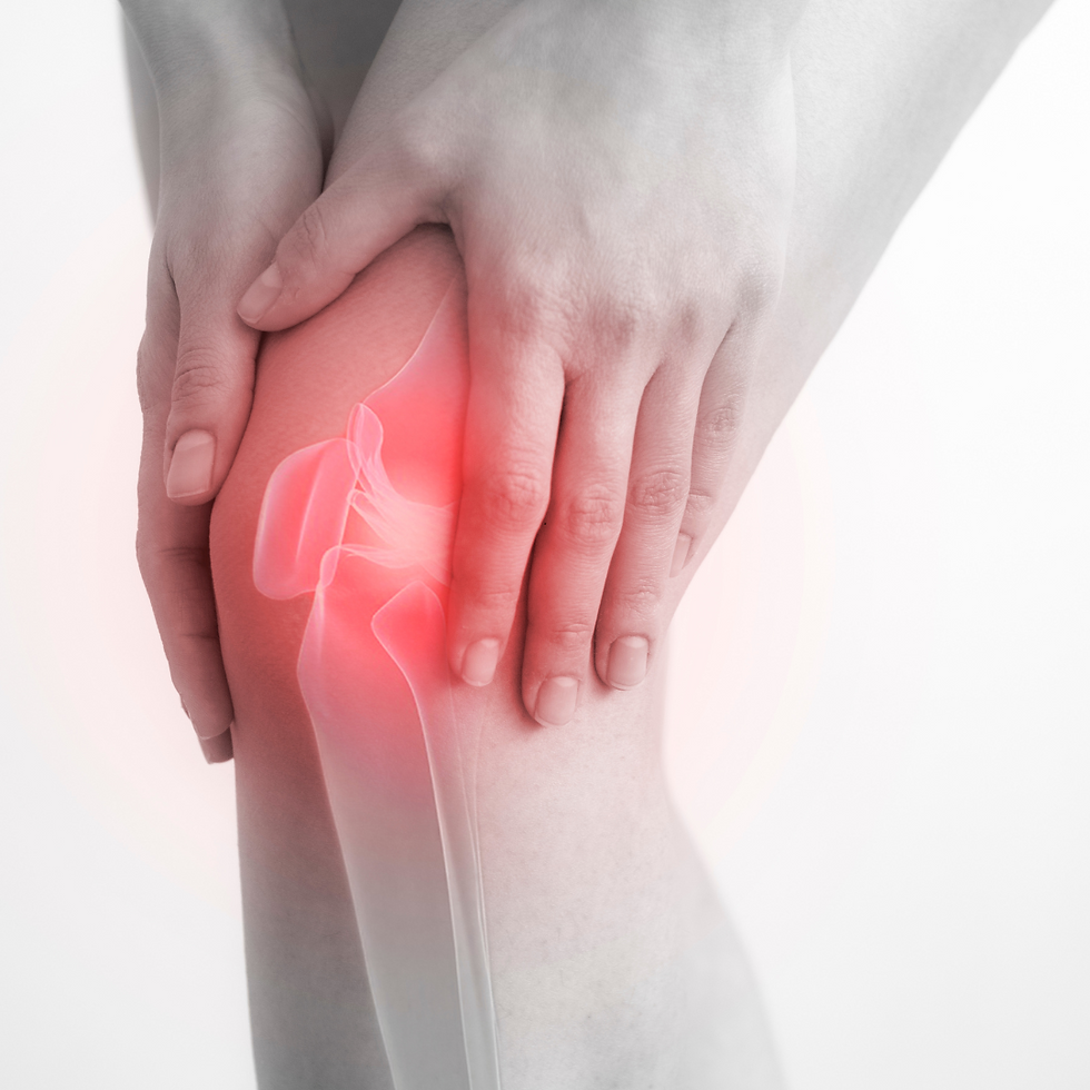 Two hands gently holding a knee with a visible red mark indicating an injury.