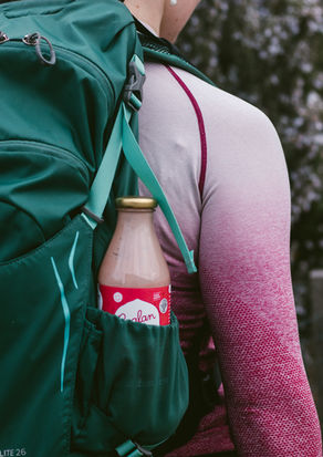 Shot Of A Bottle Of Raglan Food Co Kefir Poking Out Of The Pocket Of A Hiking Bag Worn By A Woman In A Pink Top