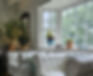 Pair of white comfort chairs in front of a sunny bay window where plants are growing
