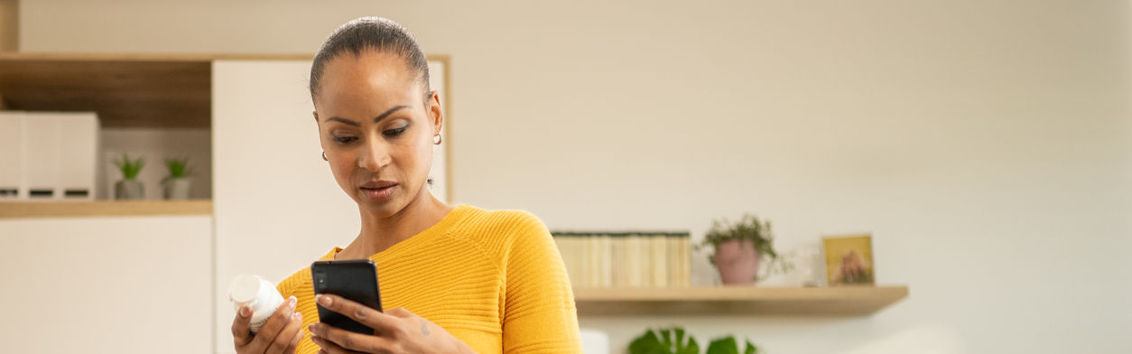 Woman-holding-pills-bottle-and-searching-instruction-on-smartphone