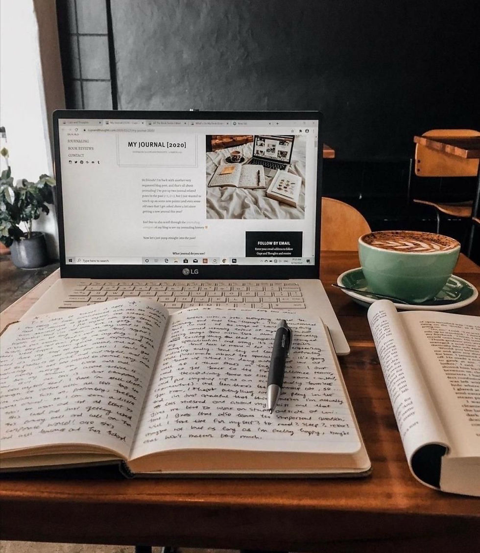 Open laptop with a website titled "My Journal [2020]," a handwritten journal, a pen, and a cappuccino on a table in a cozy café setting.