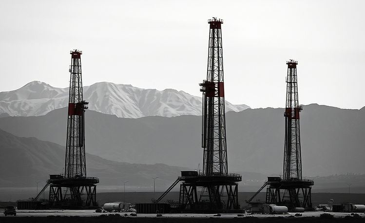 Grayscale image with subtle red highlights of three drilling rigs in a stark landscape aga