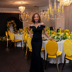 Charity Lenaé standing in front of a serpentine table setup with tall candelabras, flower garlands, and candles at a Nigerian