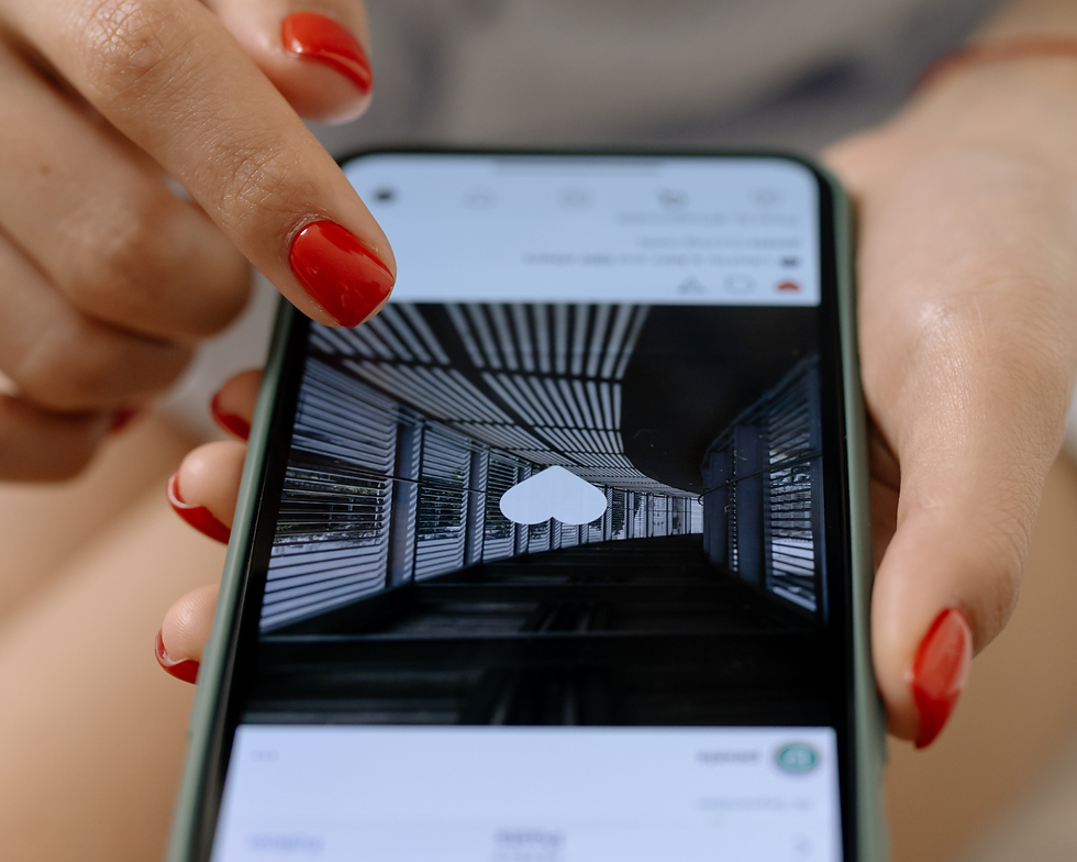 Mãos com unhas vermelhas deslizam num celular com ícone de coração branco e feed de app em corredor escuro.