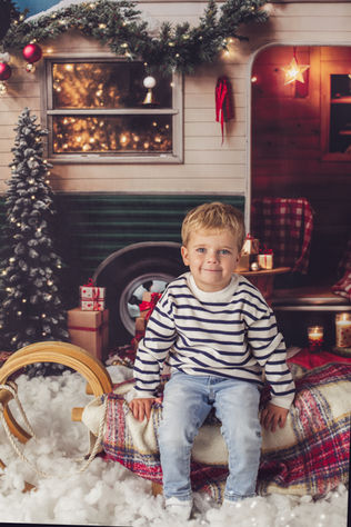 boy smiling at camera, sitting in front of a caravan in a Christmas photoshoot at Moonlion Studio, Milton Keynes