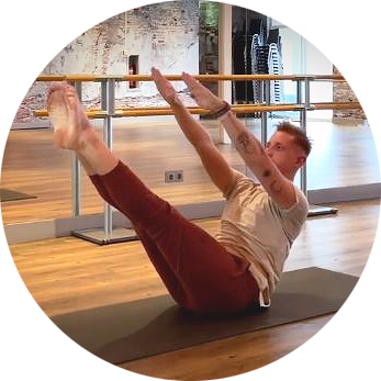 Man in pilates stance named teaser with red pants and off white coloured shirt.