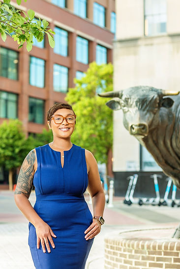 Ja'Nell shown in a blue dress in font of Major Bull, a bronze statue, in downtown Durham