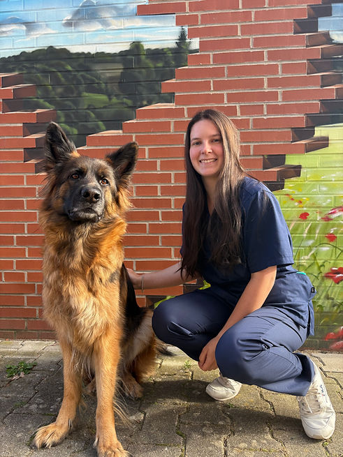 Street-Foto einer Tiermedizinischen Fachangestellten, die vor einer Backsteinmauer kniend neben einem Deutschen Schäferhund posiert.