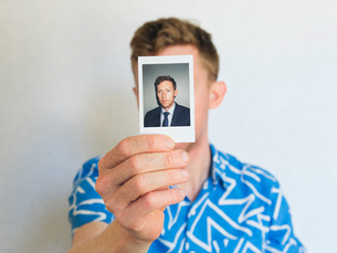 Man holding a photograph of himself dressed professionally, representing identity and life transitions