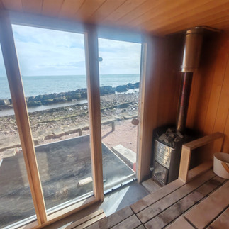 View from insdie a wooden sauna looking out through a glass wall to the sea