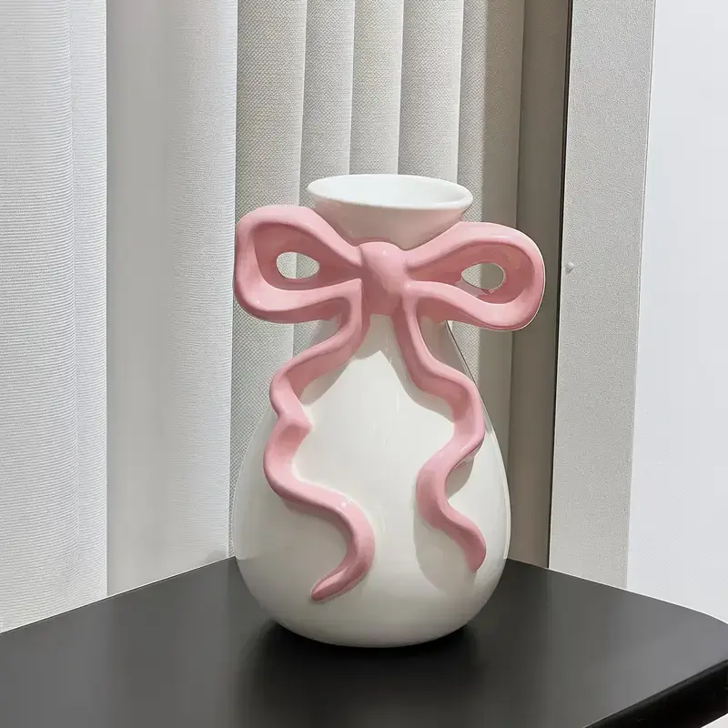 White ceramic vase with a sculpted pink bow accent, filled with dried flowers.