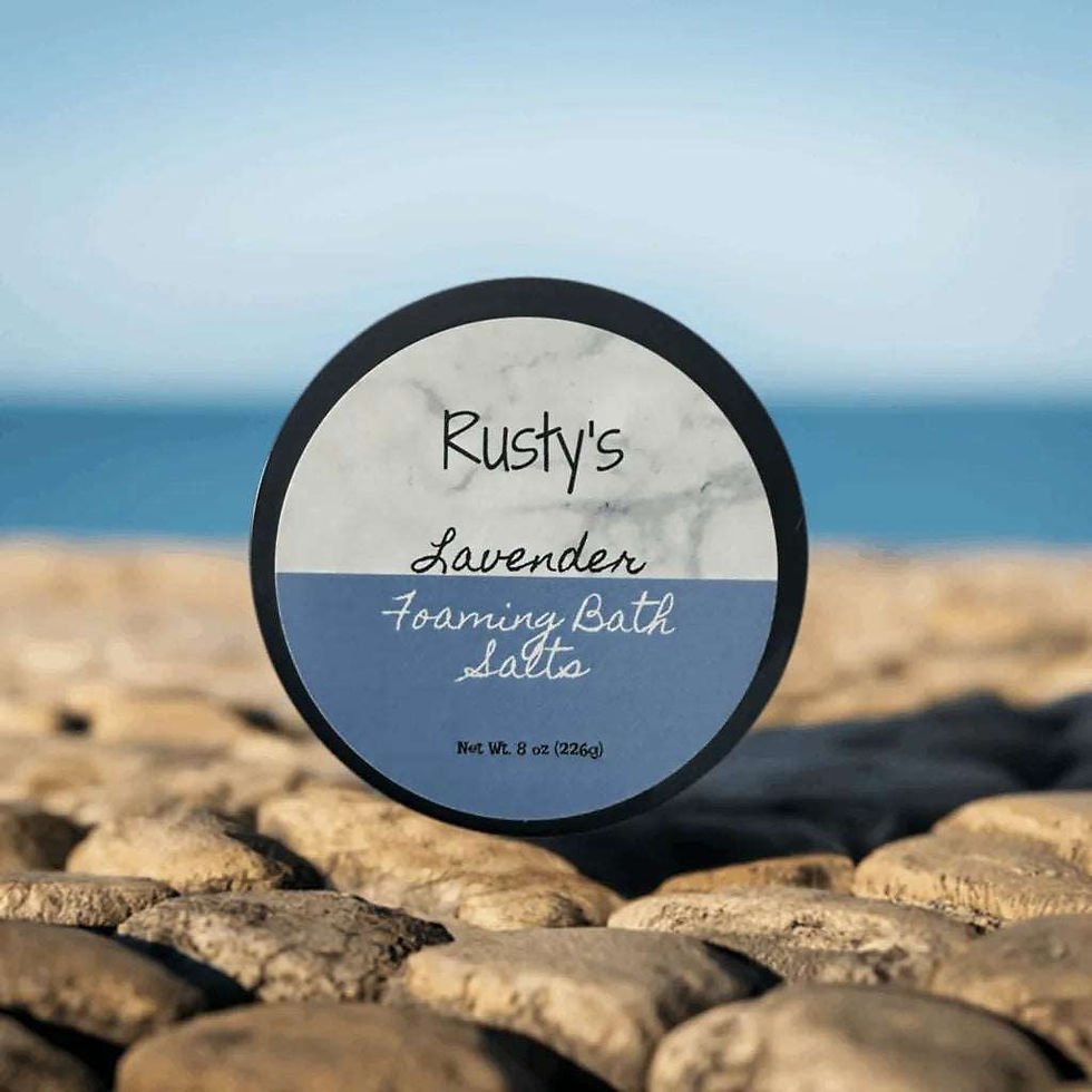 Thumbnail: Rusty's Foaming Bath Salts sit on a smooth rock, ready to provide a luxurious and relaxing bath experience. The salts are packaged in a sleek and modern container, perfect for any bathroom decor. Add these bath salts to your routine for a spa-like experience in the comfort of your own home.