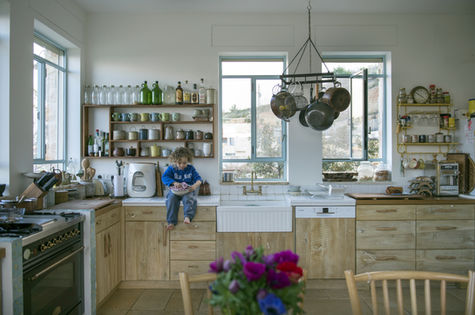 ילד יושב על השיש במטבח ליד חלון עם סירים תלויים.