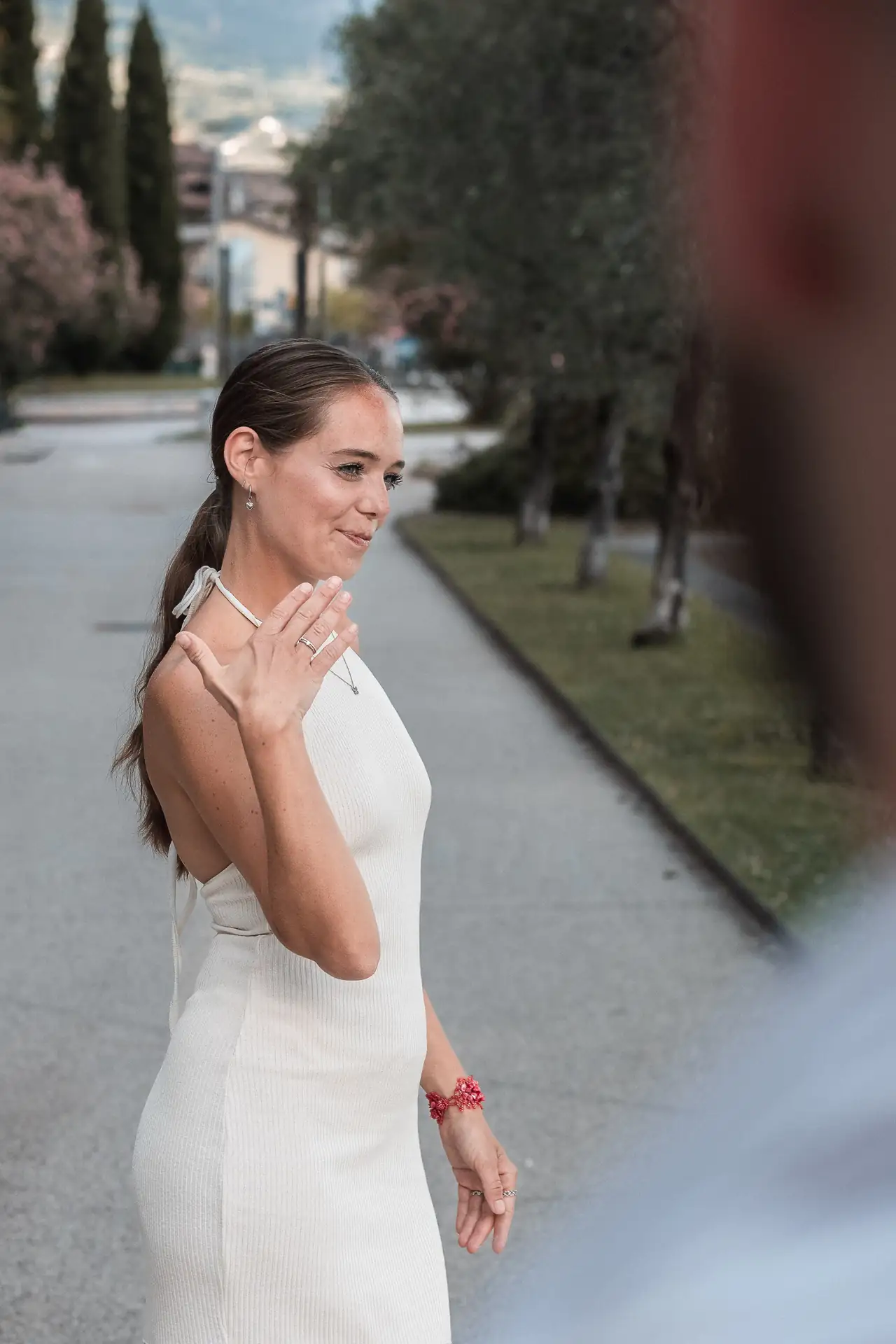 Young woman smiling while admiring her hands, showing off engagement rings, wearing a white halter dress.