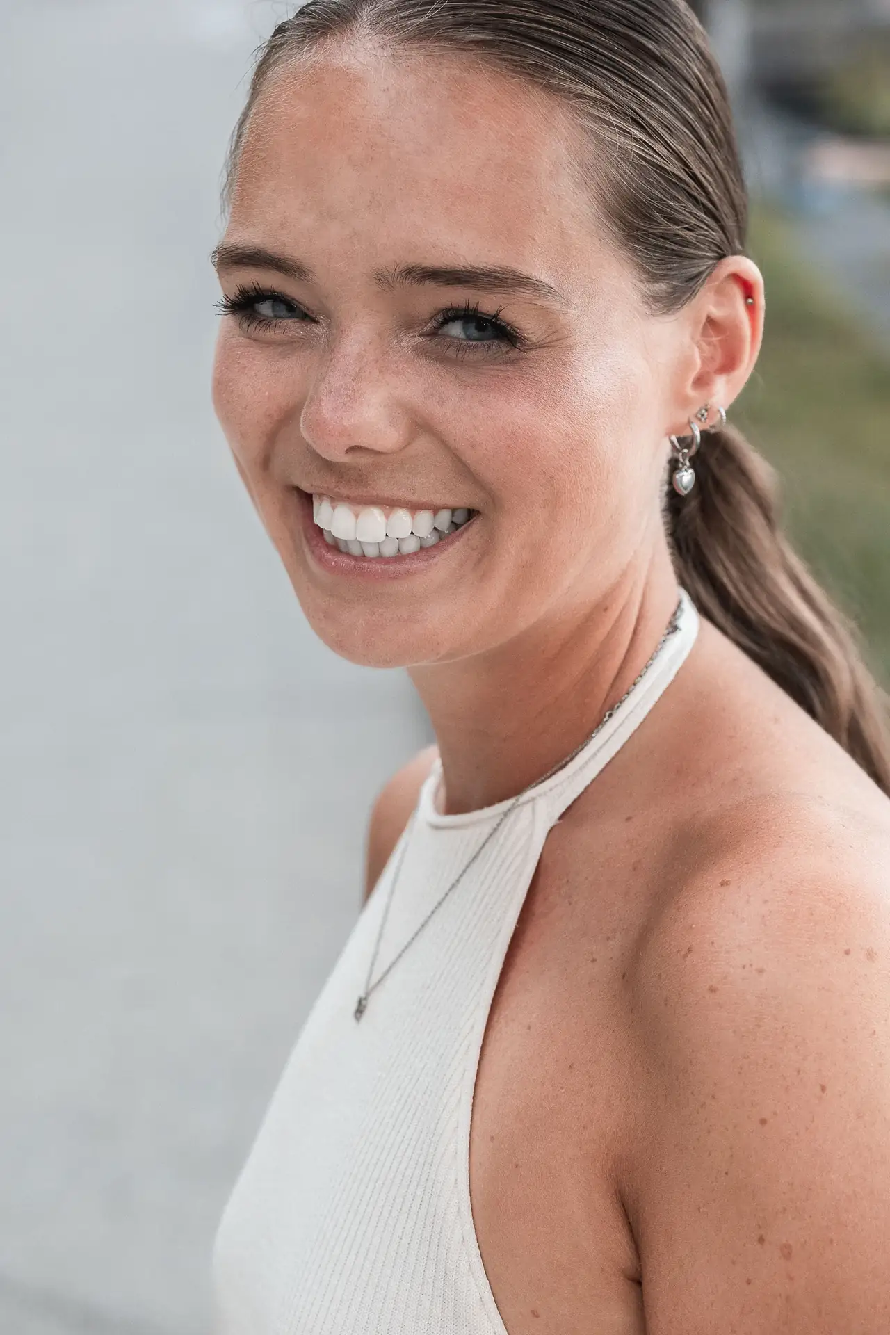 Joyful woman waving her hand with engagement ring outdoors, smiling at her partner in the background.