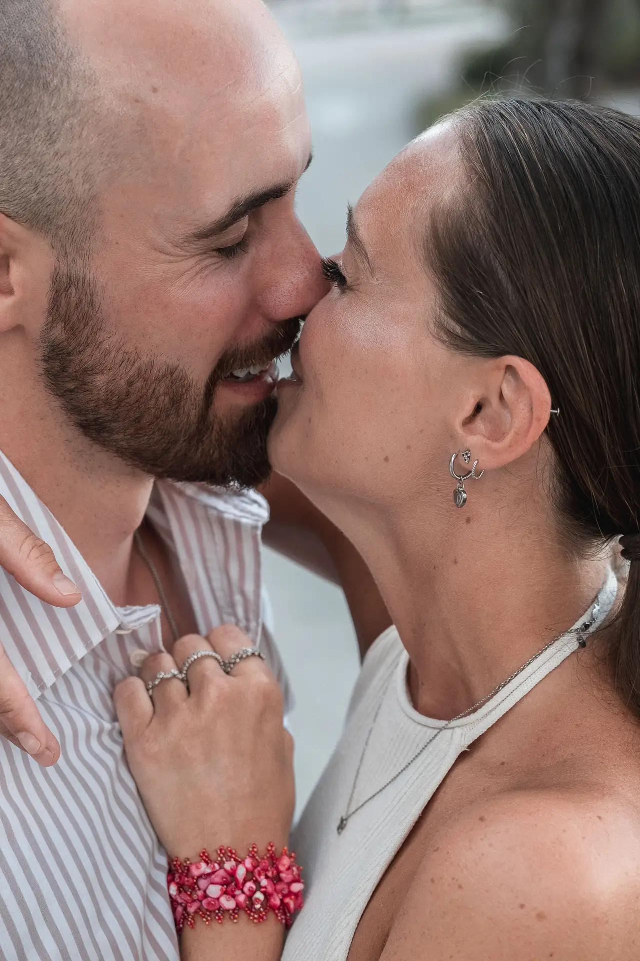 Loving couple sharing a kiss, showcasing their rings and joyful expressions during a romantic moment.