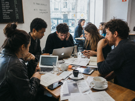 A candid documentary photograph of young founders working intensely with laptops in a modern Lisbon cafe, representing the European startup ecosystem.