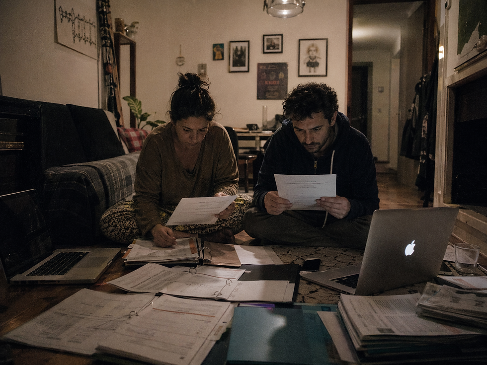 Uma fotografia realista de um casal sentado no chão rodeado por portáteis, certificados e documentos financeiros, ilustrando o pesado ónus da prova para um pedido de nacionalidade.