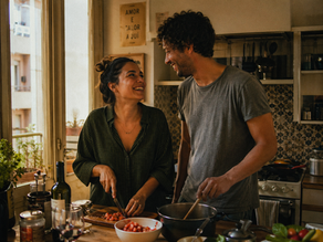 A candid documentary photograph of a diverse couple cooking together and laughing in a warm Portuguese kitchen, illustrating a genuine domestic civil partnership.
