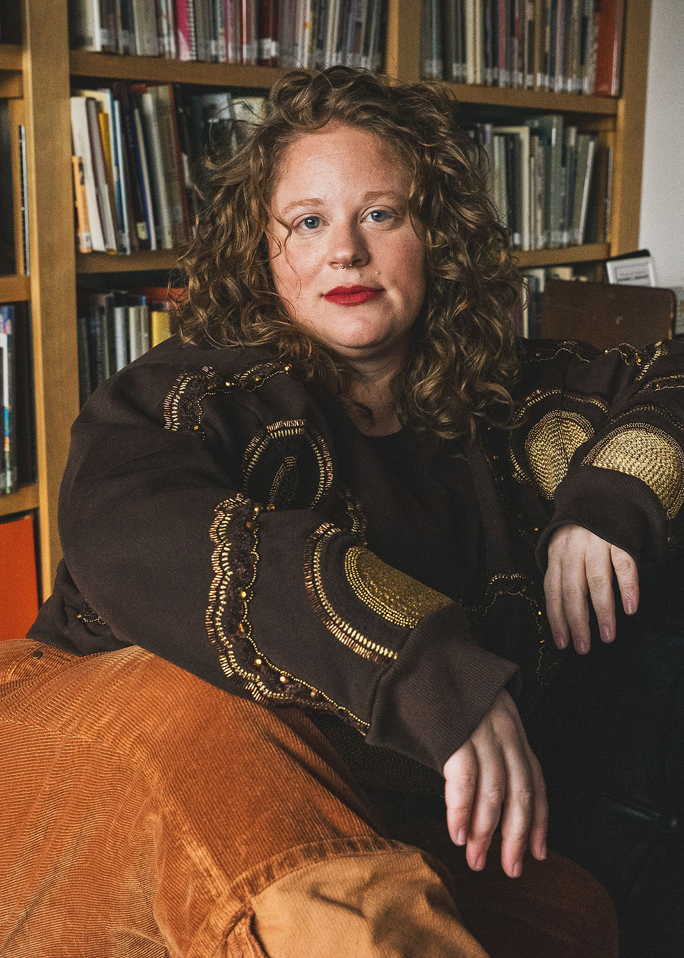 BRIGET SITTING IN THE LIBRARY AT PYRAMID ATLANTIC ART CENTER WEARING ALL BROWN WITH A TEXTURED SWEATSHIRT AND CORDUROY PANTS.