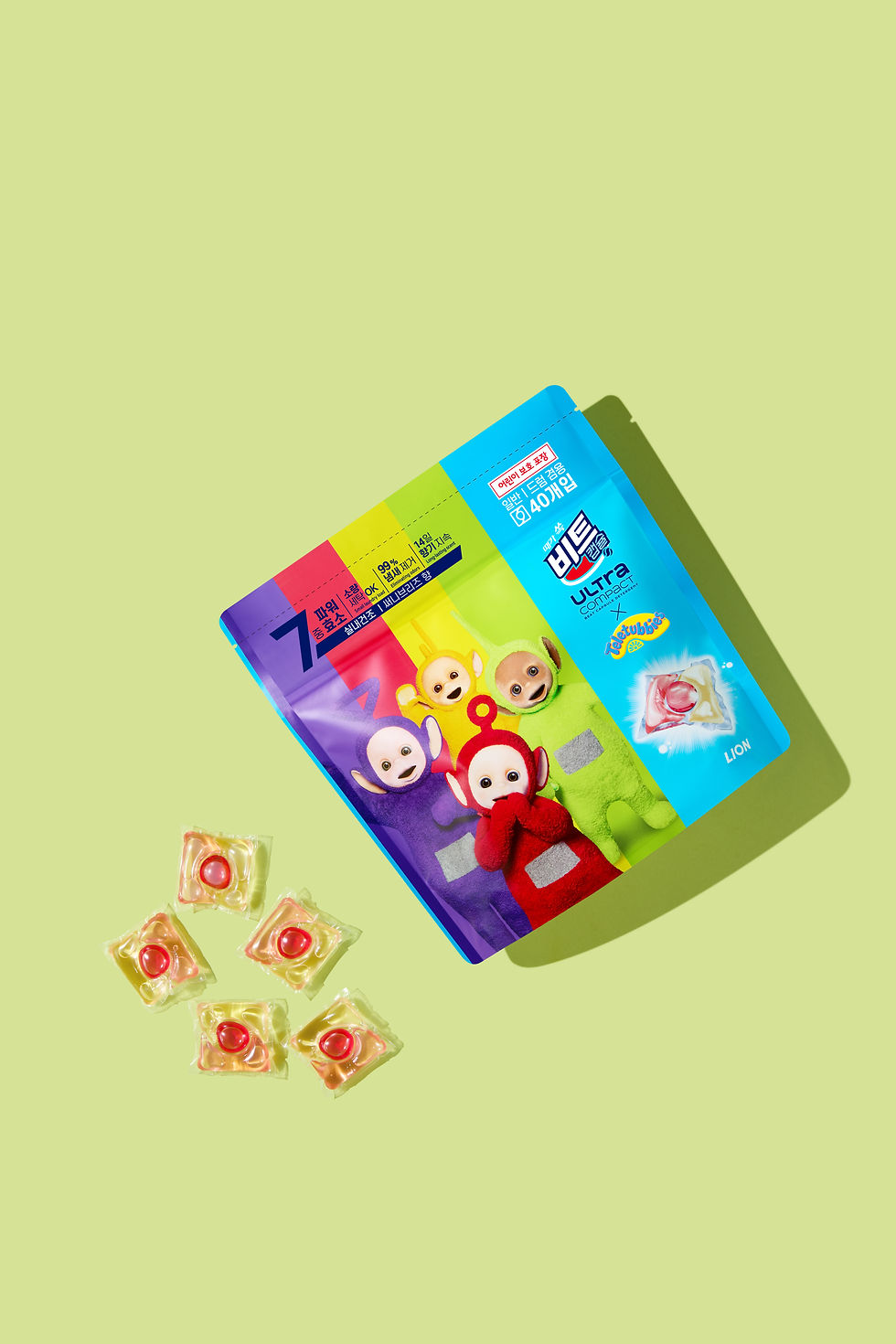 Colorful detergent packaging featuring playful characters on a light green background with six detergent pods scattered nearby.