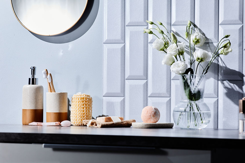 Bathroom countertop with toothbrushes, soap dispenser, exfoliating sponge, and a vase of white flowers. Clean, minimal, and bright setting.