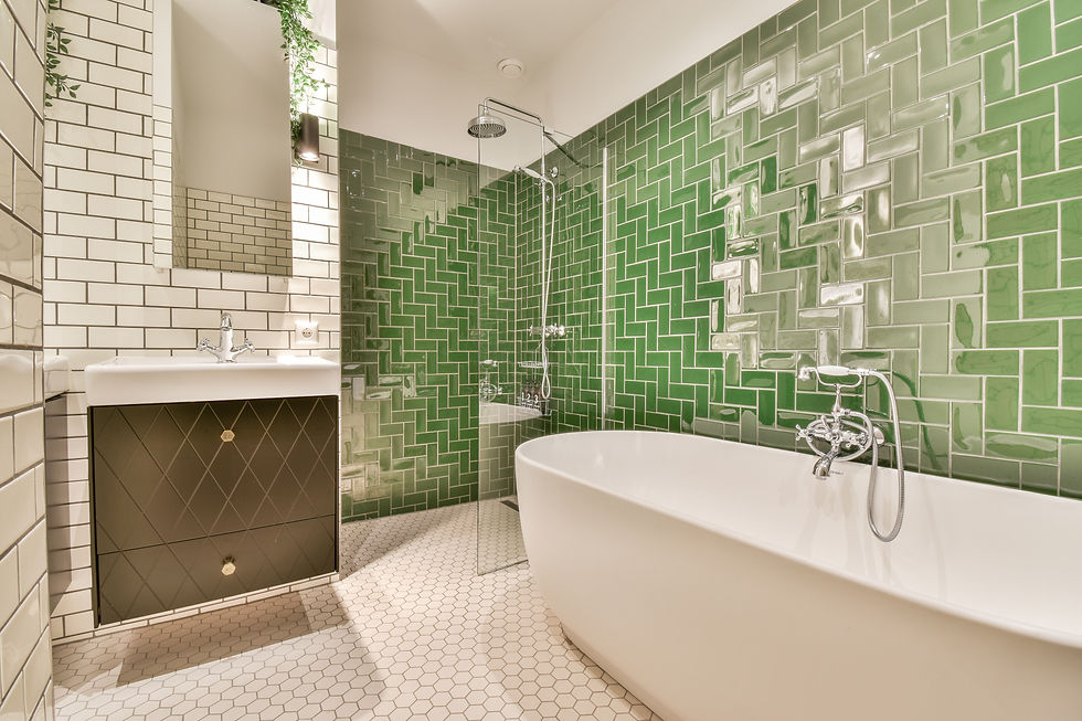 Modern bathroom with green tile walls, white bathtub, and hexagonal floor tiles. A sink with a mirror and plants add a fresh feel.