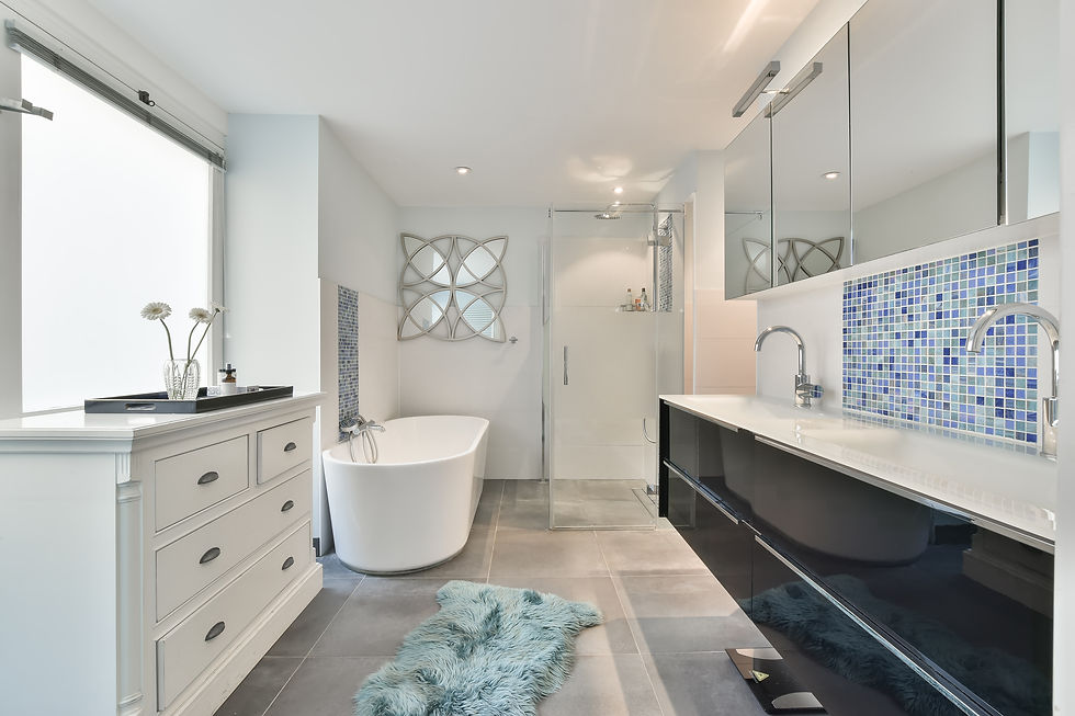 Modern bathroom with white tub, glass shower, blue mosaic tiles, and a large vanity. Soft lighting and a fluffy blue rug add a cozy feel.