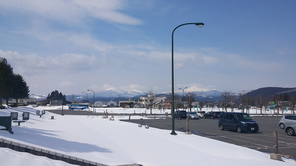 雪に覆われた駐車場と遠くの山々が広がる風景。青空の下、数台の車とバスが見える。静かで穏やかな雰囲気。