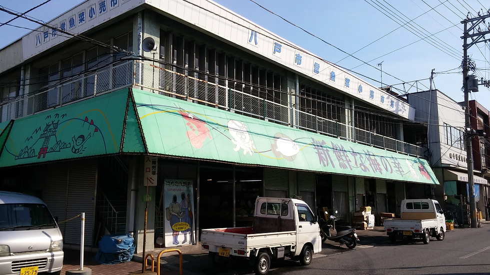 八戸市の市場の建物。緑の日よけにイラストと「新鮮な海の幸」などの文字が描かれている。駐車中の軽トラックが見える。