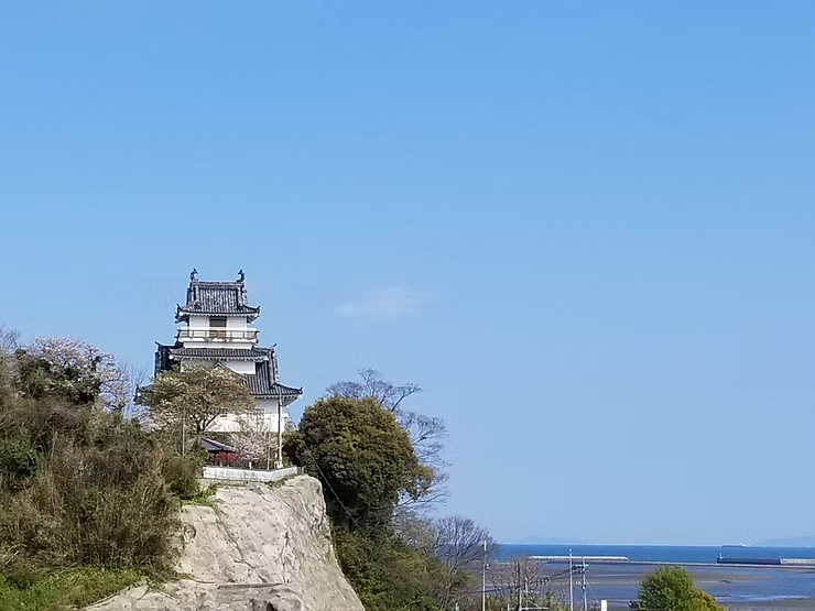 青い空と海を背景に、崖の上に立つ白い日本の城。静かな春の風景。