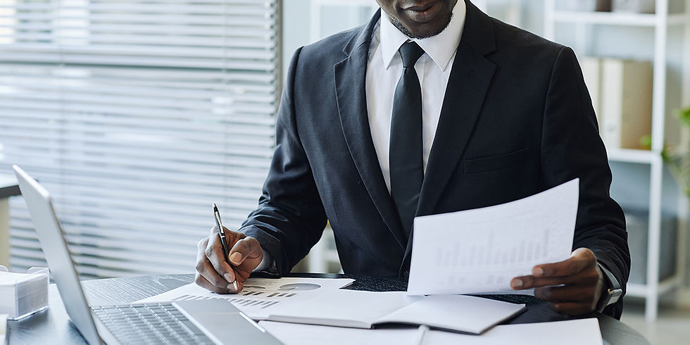 Businessman in a black suit reviews financial charts at a desk with a laptop in a bright office.