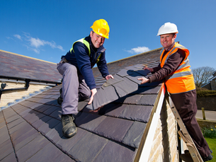 Two professional roofers in hard hats installing new slate roofing tiles during a residential roof replacement project.