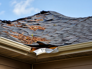 Residential roof with significant wind damage and missing shingles after a storm.
